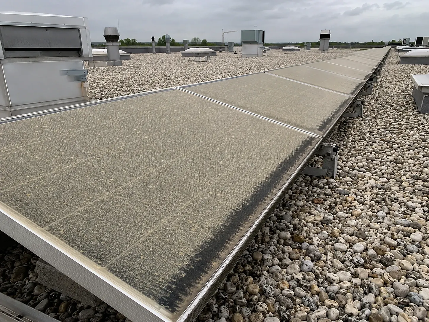 Solarmodule auf einem gewerblichen Flachdach mit Kiesauflage, halb noch mit Schmutzfilm bedeckt.